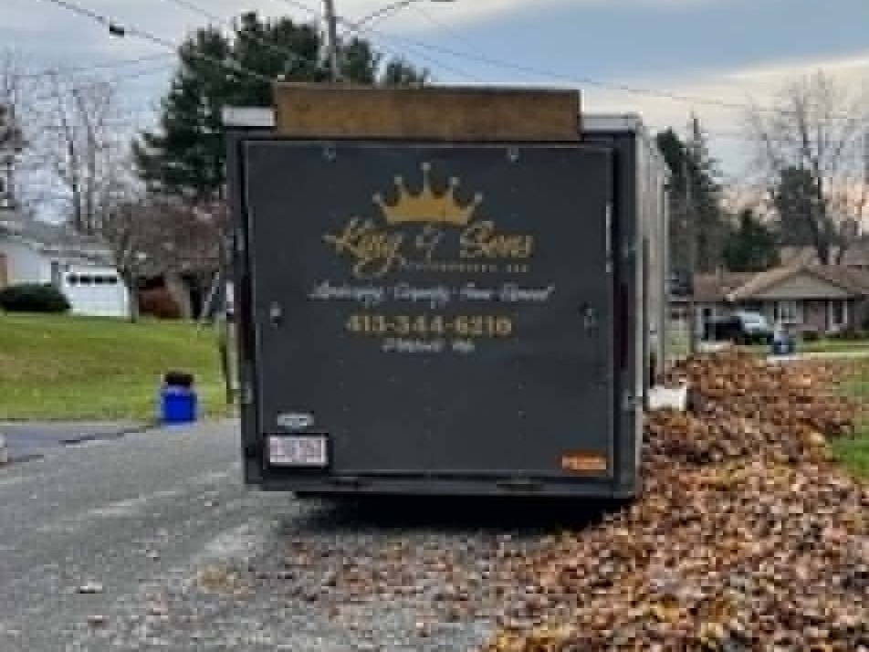 The King & Sons crown-logo trailer centered on a fall cleanup job, leaf pile swept up behind it