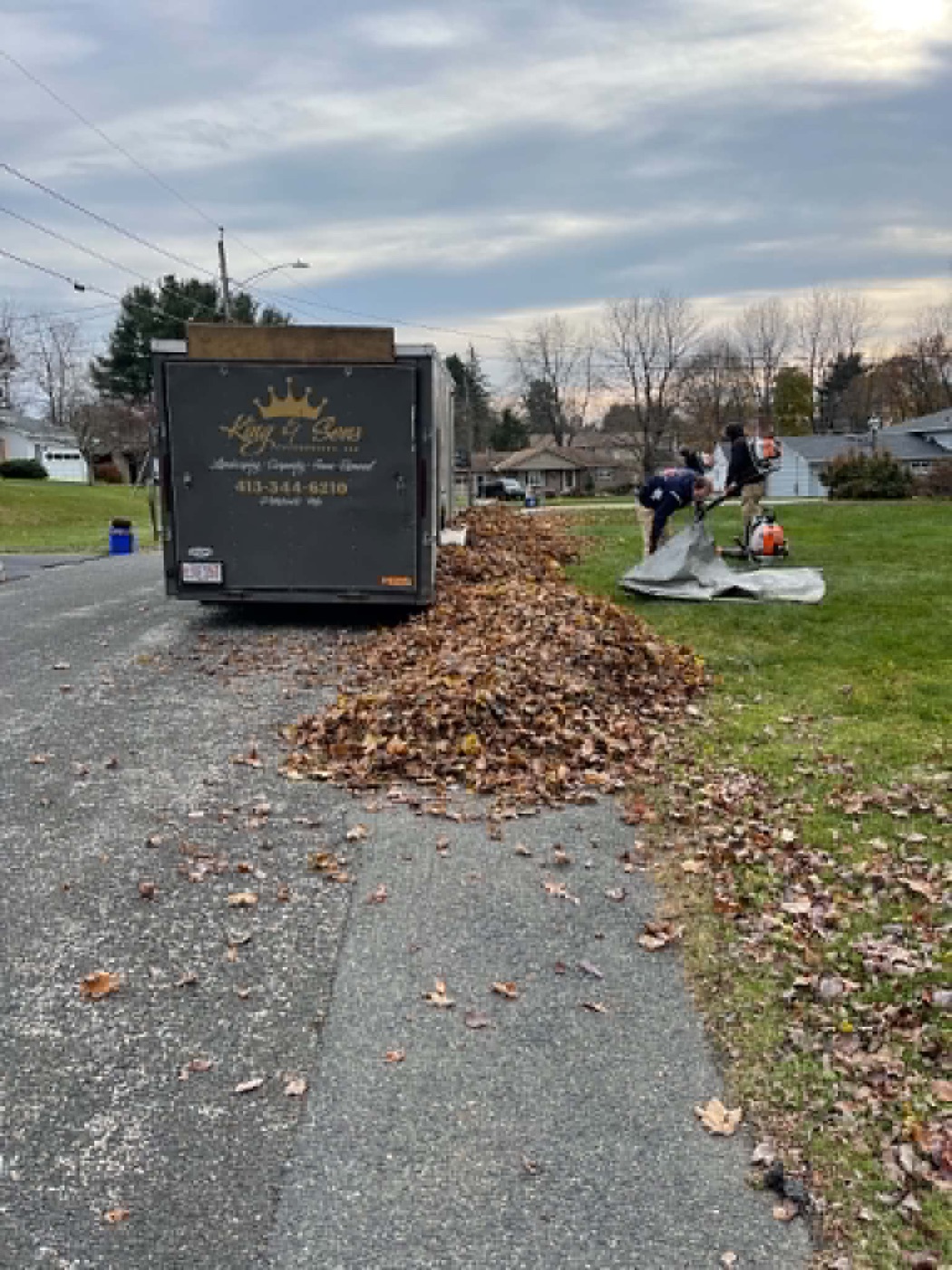 King & Sons crew blowing a long leaf pile onto a tarp beside the branded company trailer