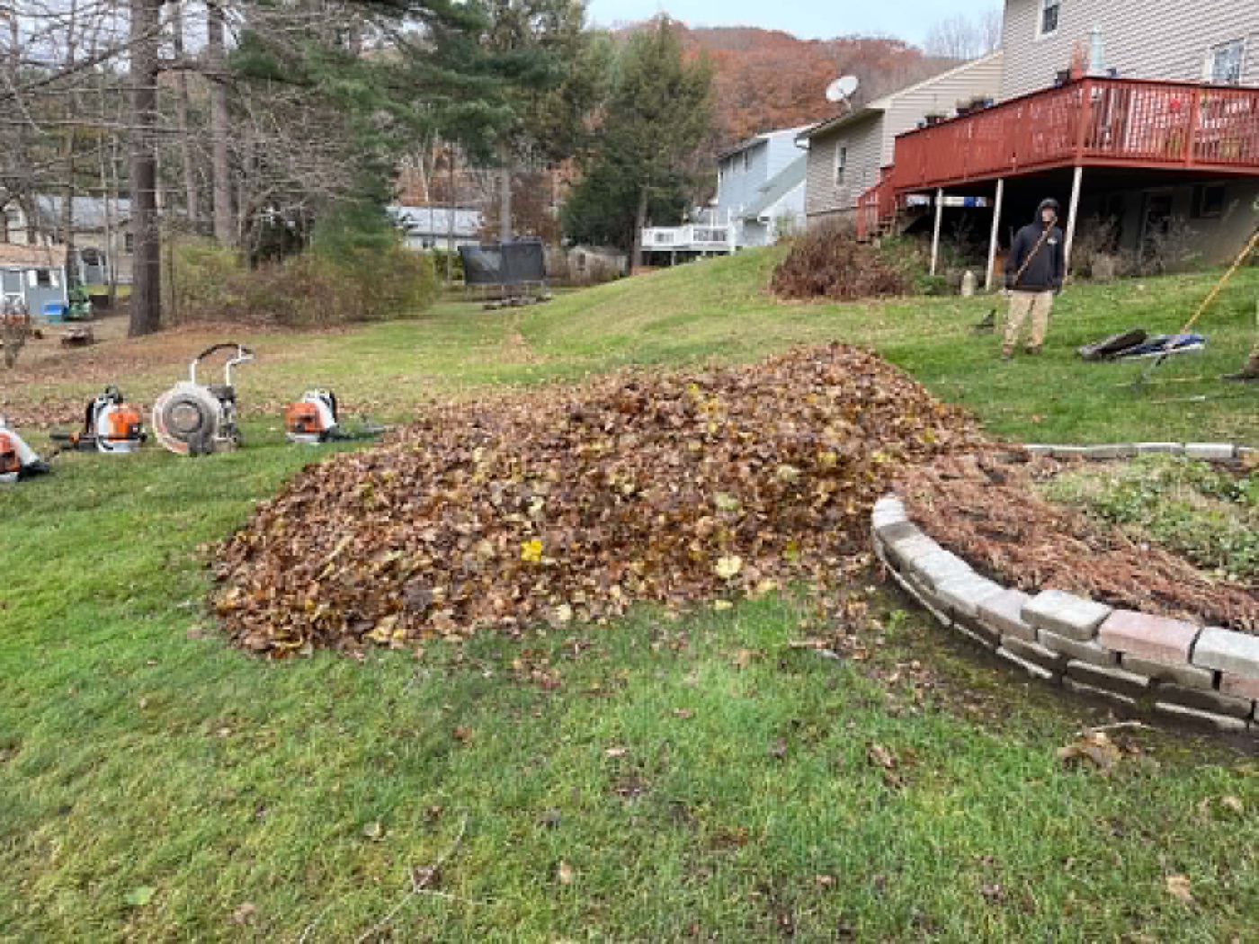 Crew member beside a large leaf pile with backpack blowers staged on the lawn