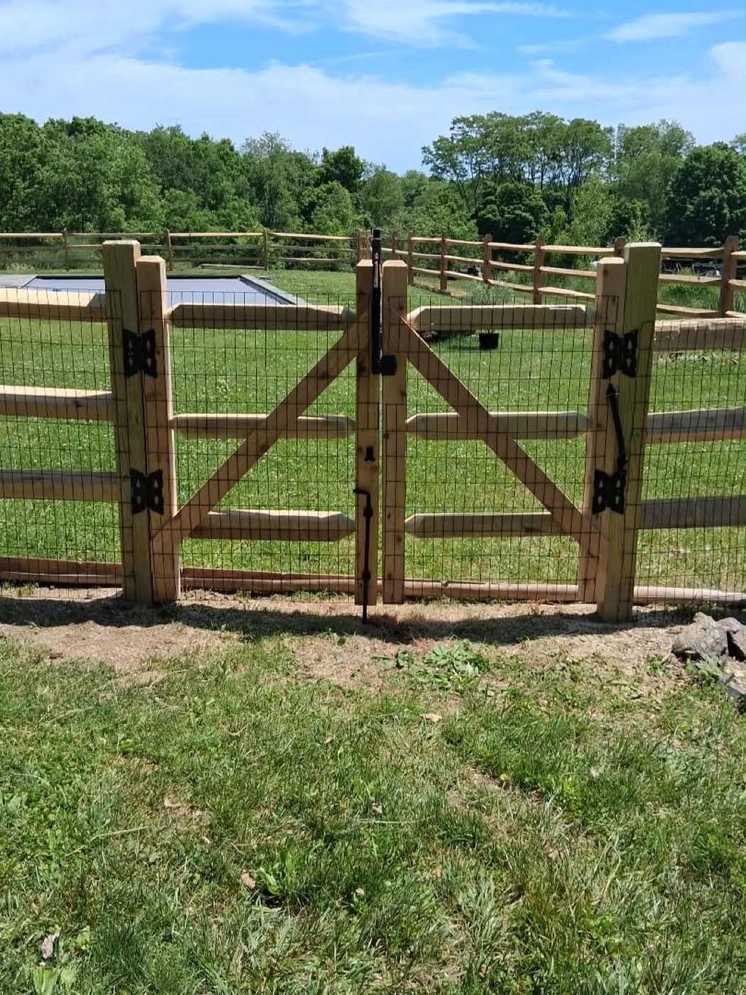 Split-rail paddock fence with welded-wire backing and a wooden double gate