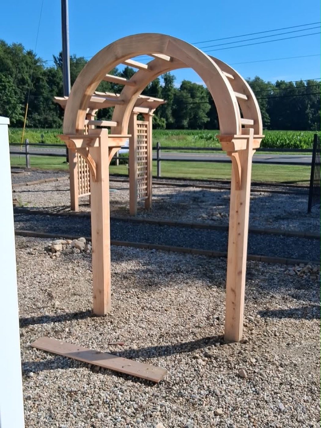 Arched cedar garden arbor with lattice side panels, freshly installed on a gravel pad