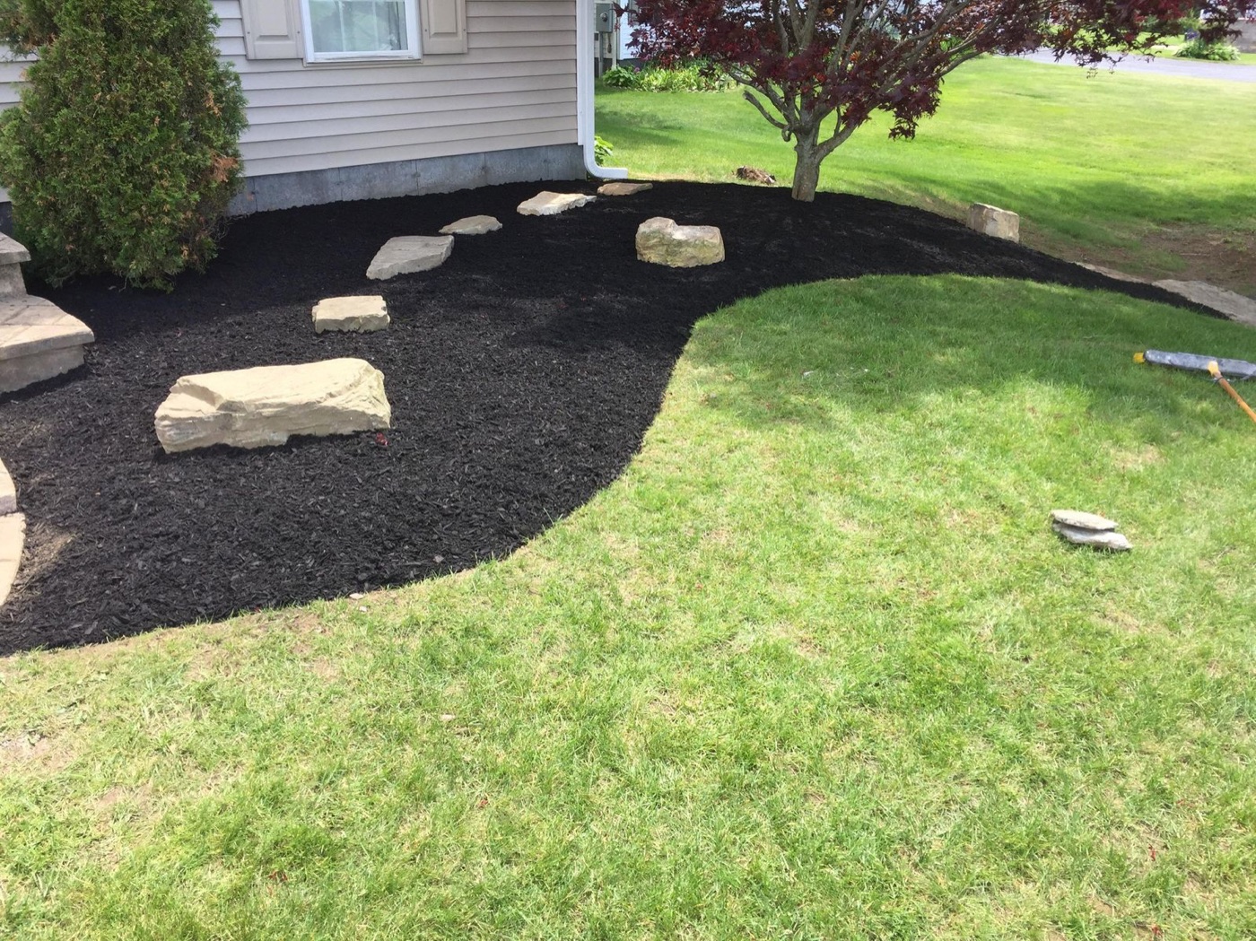 Black mulch bed with fieldstone boulders and stepping stones set into the lawn