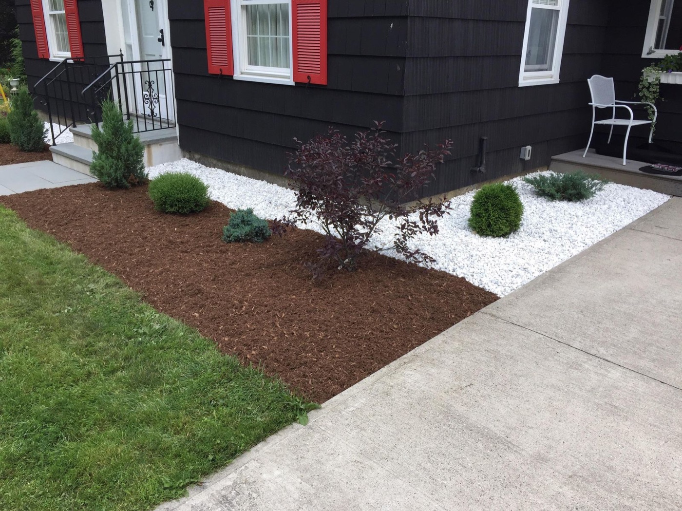Black mulch bed and white stone border wrapping a dark-sided home