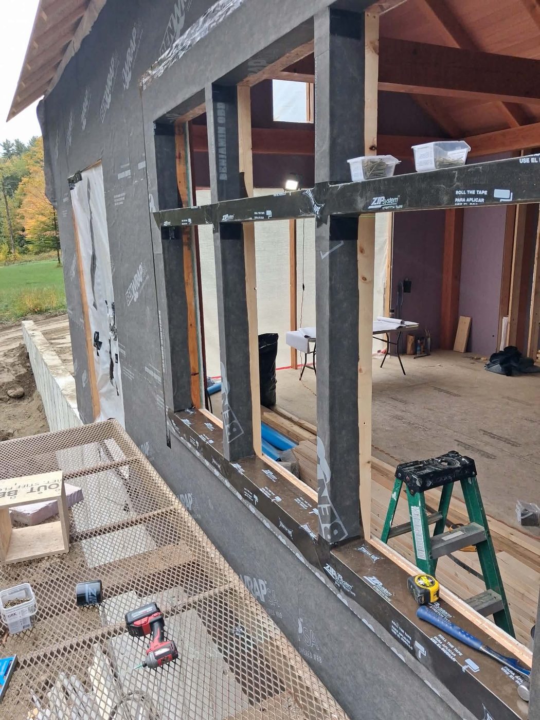 Framed window openings in a house-wrapped wall, with flashing tape on the sills and sides, seen from the scaffold staging