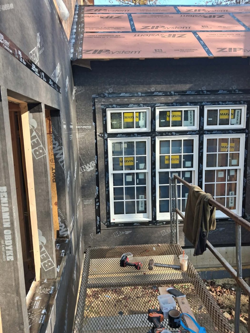 A bank of six new windows, three over three, taped into the house wrap, seen from the scaffold staging